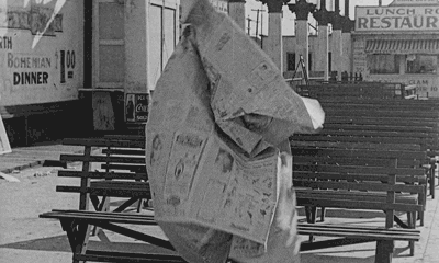A gif of a person holding an enormous piece of newspaper, which keeps tangling and nearly flying away